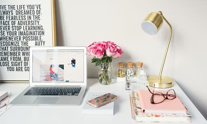 A laptop, roses and notebooks on a bright desk